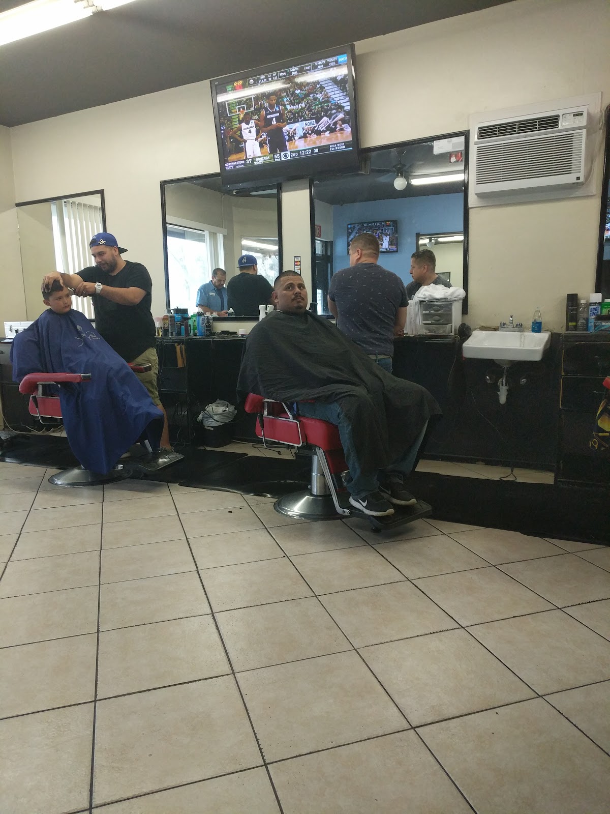 Two barbers working on clients with the TVs on